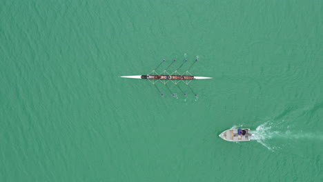 Following-a-rowing-team-aerial-top-view-training-with-a-coach-on-a-boat-lake